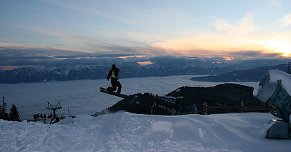 Snowboarder auf der Gerlitzen Alpe im Sprung vor dem Sonnenuntergang im Skiurlaub.