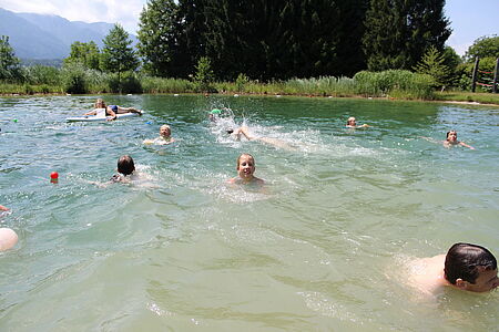 Badesee mit Gästen in der Hausgalerie von der Sommerreise der Ferienanlage Forellenhof in Kärnten in Österreich am Faaker See.