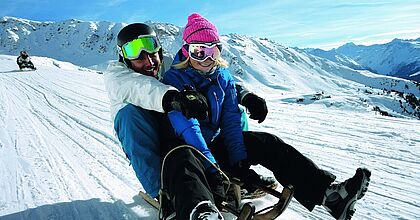 Zwei Menschen, die im Skiurlaub in Frankreich die verschneite Piste rodeln.