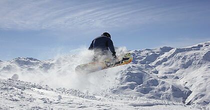 Snowboarder im Sprung. Im Hintergrund erstrecken sich die verscneiten Berge